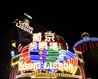 Bright neon signs in multiple colors illuminate the night, prominently displaying the name 'Casino Lisboa' alongside signage in Chinese characters. The lights form intricate patterns and vibrant displays, creating a lively and energetic atmosphere.