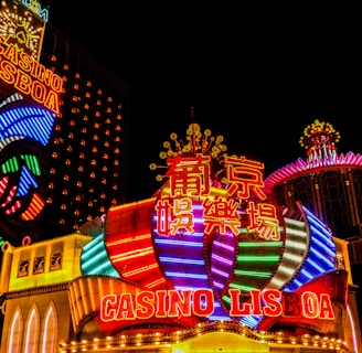 Bright neon lights and colorful signage adorn the exterior of Casino Lisboa, creating a vibrant and lively atmosphere. The façade features bold, multicolored designs with a mix of English and Chinese characters prominently displayed. The lights form intricate patterns and shapes, contributing to the energetic ambiance of the scene.